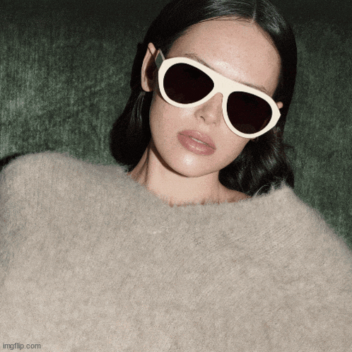 a woman wearing sunglasses and a sweater is displayed on a green background
