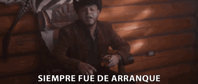 a man in a cowboy hat sits in a chair with siempre fue de arranque written in white
