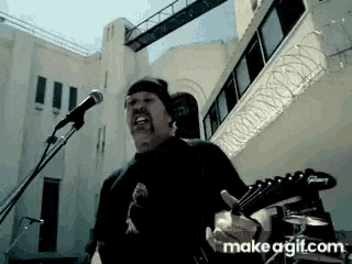 a man singing into a microphone and playing a guitar with makeagif.com in the lower right corner