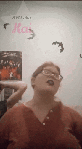 a woman wearing glasses and black lipstick is standing in front of a wall with bats and a poster that says avo aka ka