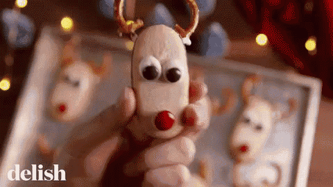 a person is holding a cookie in the shape of a reindeer with a red nose .