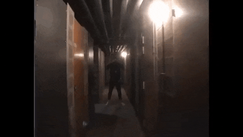 a man is standing in a dark hallway with a light on the wall .