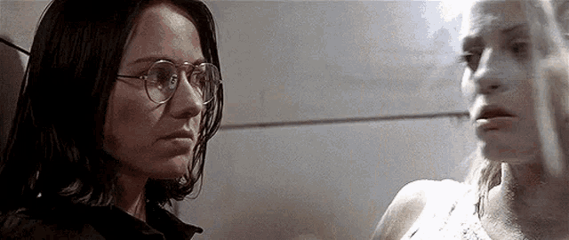 two women wearing glasses are looking at each other in a bathroom .