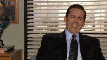 a man in a suit and tie laughs with his eyes closed