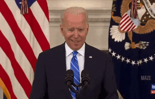 a man in a suit and tie stands in front of microphones