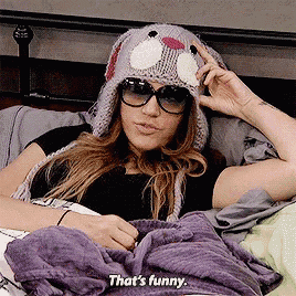 a woman wearing a knitted hat and sunglasses is laying in bed and saying that 's funny