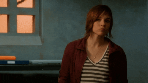 a woman wearing a striped shirt and a red jacket looks at the camera