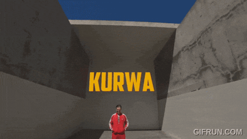 a man in a red adidas jacket stands in front of a wall with the word kurwa on it