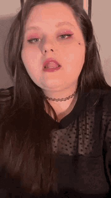 a woman with pink eye shadow and a choker shows her tongue
