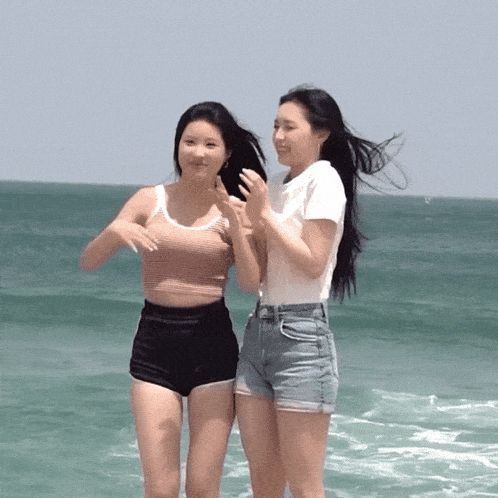 two women are standing on the beach and one is wearing a white shirt