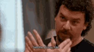 a man with curly hair and a beard is holding his hands up in front of his face .