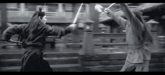 a black and white photo of two men fighting with swords in the rain .