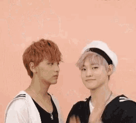 two young men are standing next to each other on a pink background . one of the men has pink hair and the other has red hair .