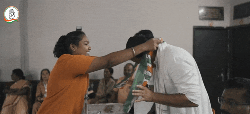 a woman in an orange shirt is touching a man 's forehead