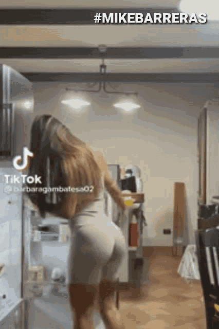 a woman is dancing in front of a refrigerator in a kitchen with a tiktok video .