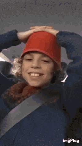 a young boy wearing a red hat is smiling while holding a red cup on his head .