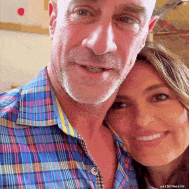 a man and a woman are posing for a picture and the man is wearing a blue plaid shirt