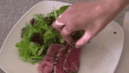 a person is putting meat on a plate with lettuce .