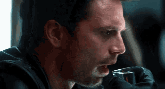 a man in a black jacket is drinking from a glass .