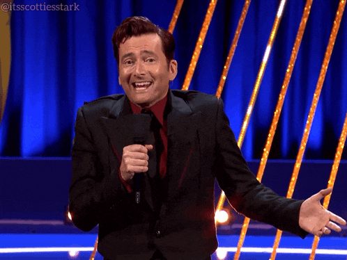 a man in a black suit and red tie is holding a microphone and laughing