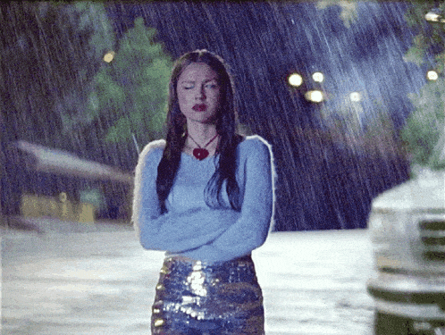 a woman in a blue sweater is standing in the rain