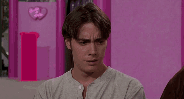 a man in a grey shirt is sitting in front of a pink wall