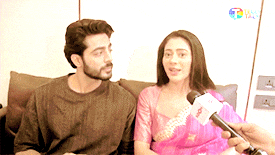 a man and woman are sitting on a couch being interviewed by a reporter