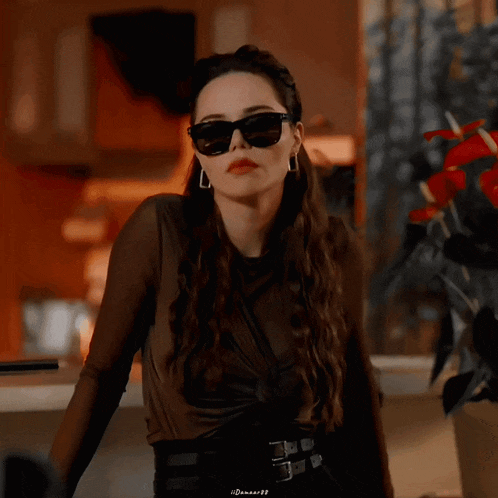 a woman wearing sunglasses and earrings is standing in front of a vase of flowers