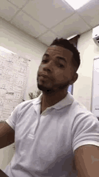 a man in a white polo shirt is taking a selfie in a room .
