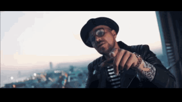 a man wearing glasses and a hat is pointing at something