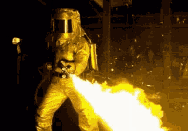 a man in a protective suit is holding a flamethrower .