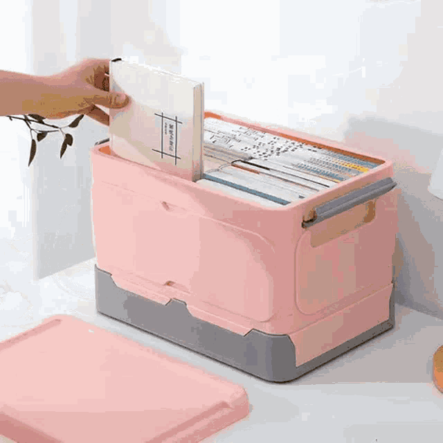 a person is taking a book out of a pink plastic bin