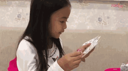 a little girl is sitting at a table looking at a piece of paper ..