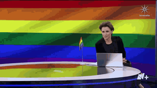 a woman sitting at a desk with a laptop in front of a rainbow flag that says las estrellas on it
