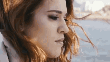 a close up of a woman 's face with her hair blowing in the wind and looking at the camera .