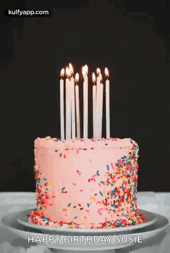 a pink birthday cake with candles and sprinkles on a white plate .