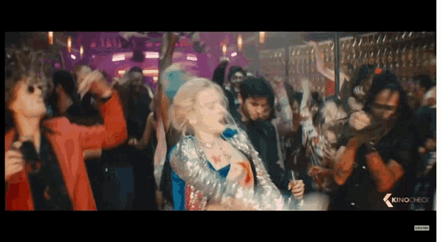 a woman in a sequined jacket is dancing in front of a crowd with the word kino on the bottom left
