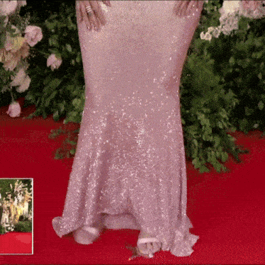 a woman in a pink sequined dress is standing on a red carpet with flowers in the background