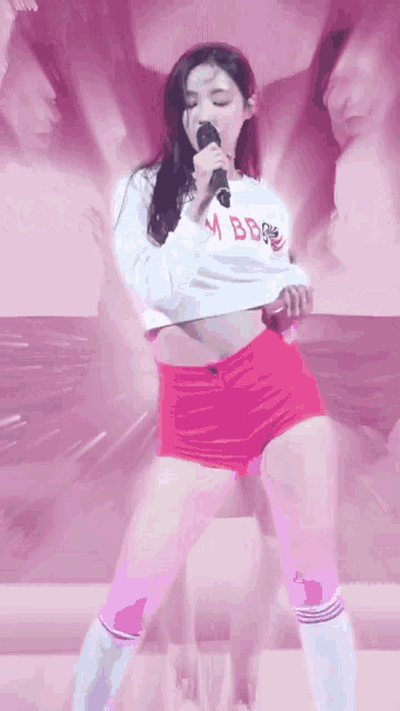 a woman is singing into a microphone while wearing a white crop top and red shorts .