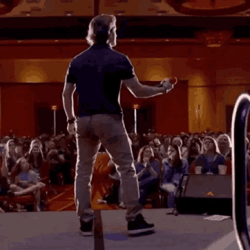 a man is standing on a stage in front of a crowd of people holding a microphone .