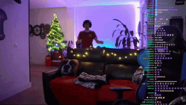 a man in a red adidas shirt is dancing on a couch in front of a christmas tree