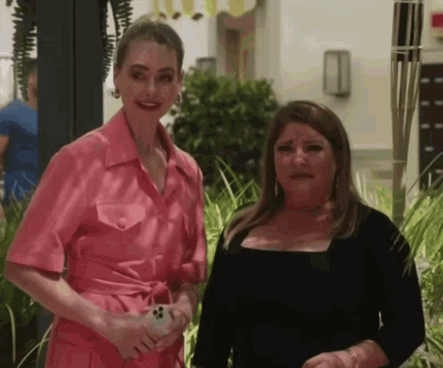 a woman in a pink dress stands next to a woman in a black top