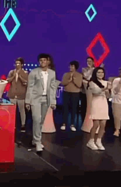 a man in a suit is walking on a stage with a group of people applauding