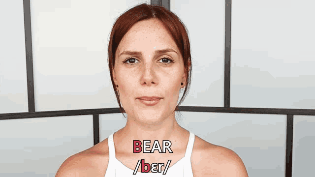a woman with red hair and freckles is wearing a white tank top that says bear on it