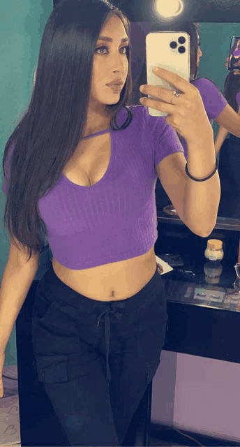 a woman in a purple crop top is taking a selfie in front of a mirror