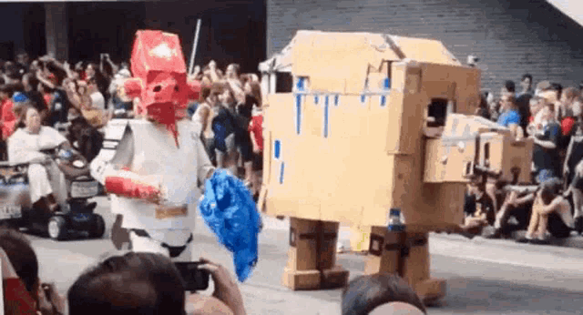 two cardboard robots are walking down a street in front of a crowd of people