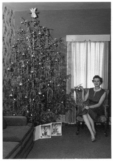 a woman is sitting in front of a christmas tree holding a christmas ornament