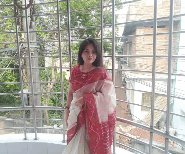 a woman in a red and white saree is standing in front of a fence