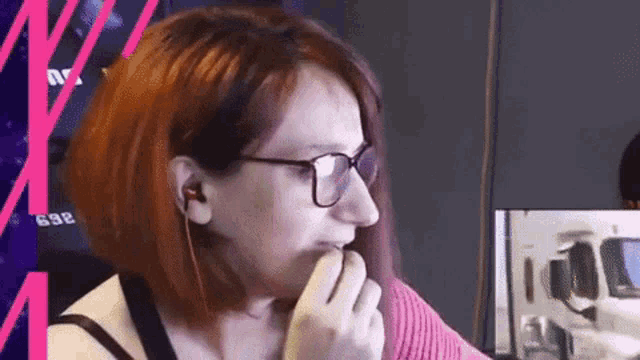 a woman with red hair and glasses is eating a banana in front of a computer monitor .