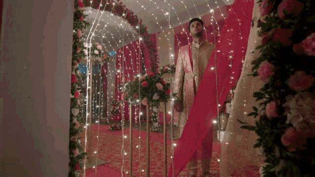 a man in a wedding dress is walking through a tunnel of flowers and lights